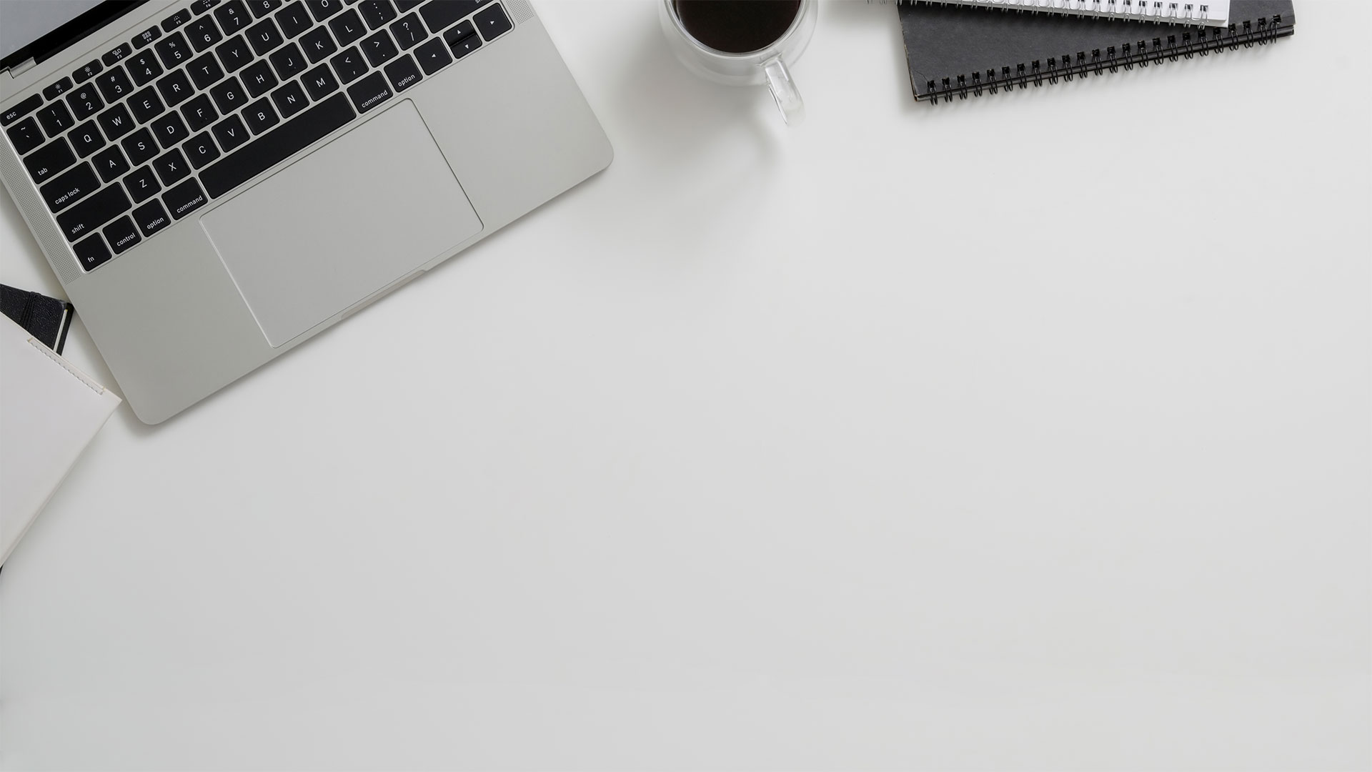 Laptop, cup of coffee and notepads on a tidy, white desk.