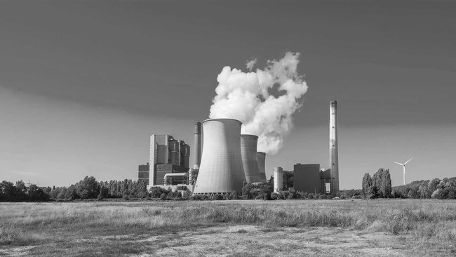 Power station with steaming cooling towers and wind turbine in a rural setting in black and white.