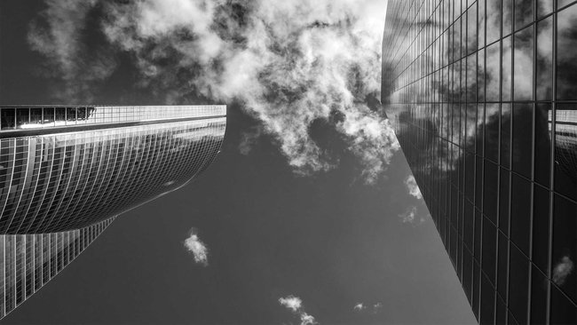 View upwards to two skyscrapers with reflecting glass facades and clouds.