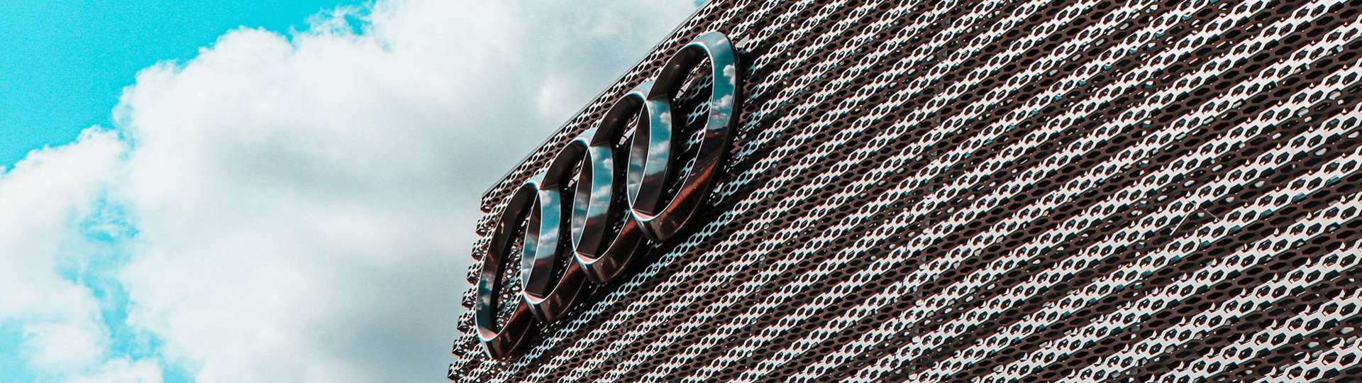 Audi logo on a modern building in front of a blue sky with white clouds.