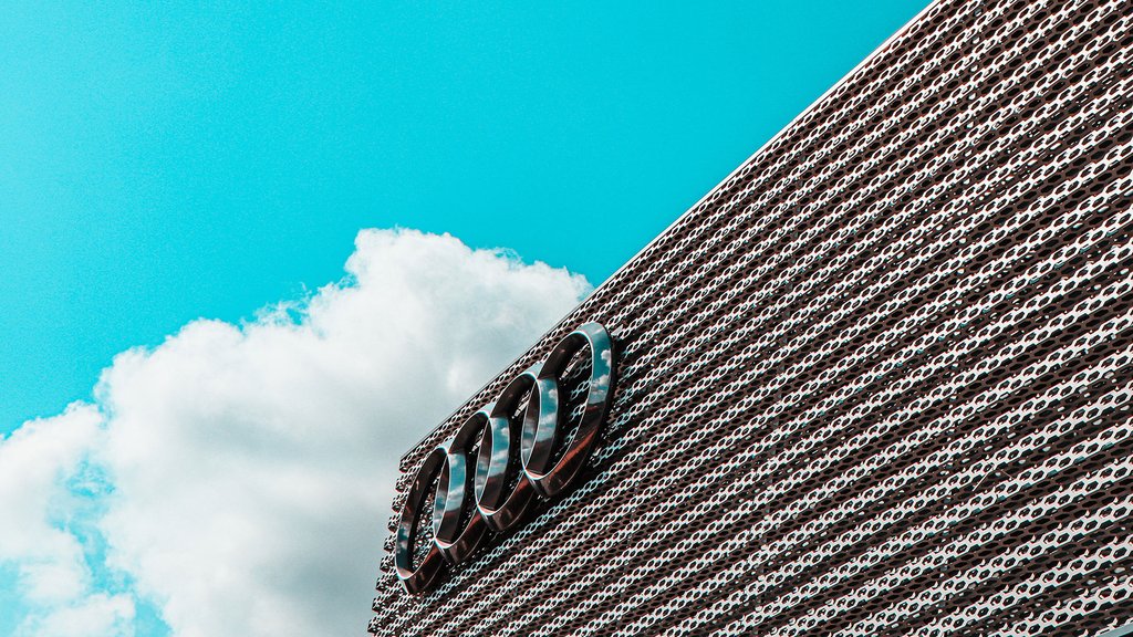Audi logo on a modern building in front of a blue sky with white clouds.