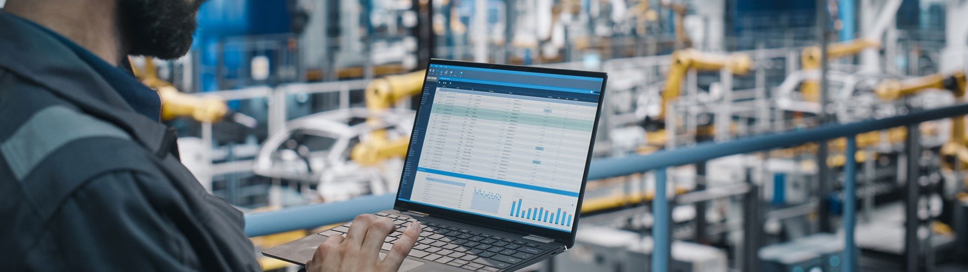 Engineer with laptop monitors production data on a modern factory floor.