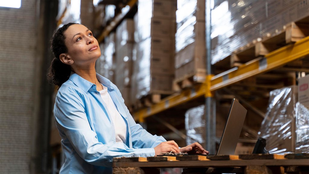 Woman working on a laptop in a warehouse an she is looking up thoughtfully.