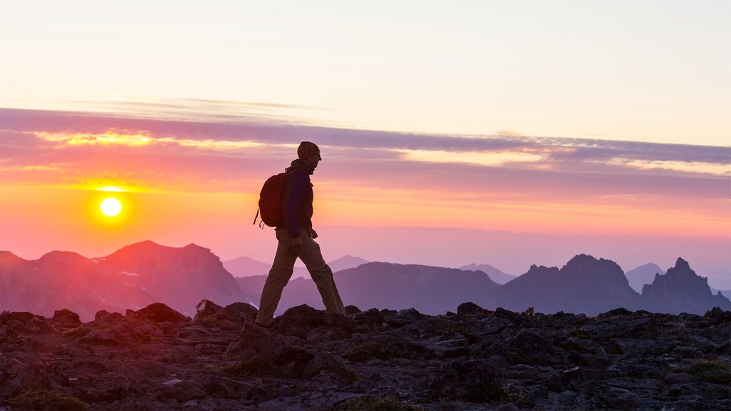 Person hiking at sunset on a rocky mountain landscape with mountain peaks in the background.