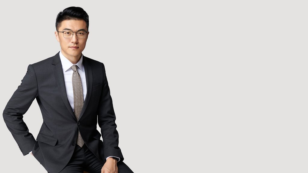 A portrait picture of Hao in a black suit against a gray background.