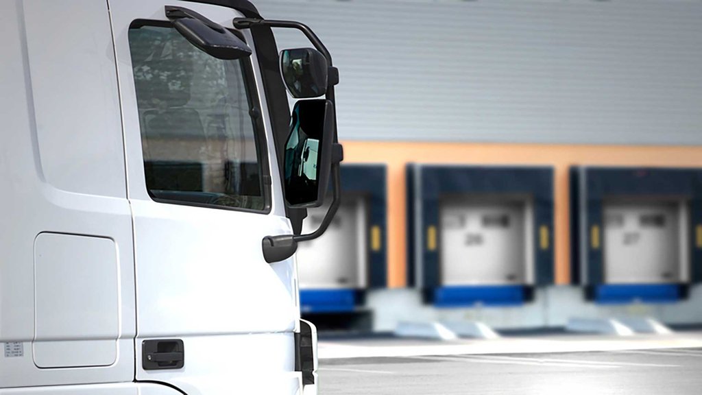 White truck side view in front of a loading ramp of a logistics center.