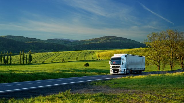 White truck on a country road, surrounded by fields and hills, for sustainable logistics.