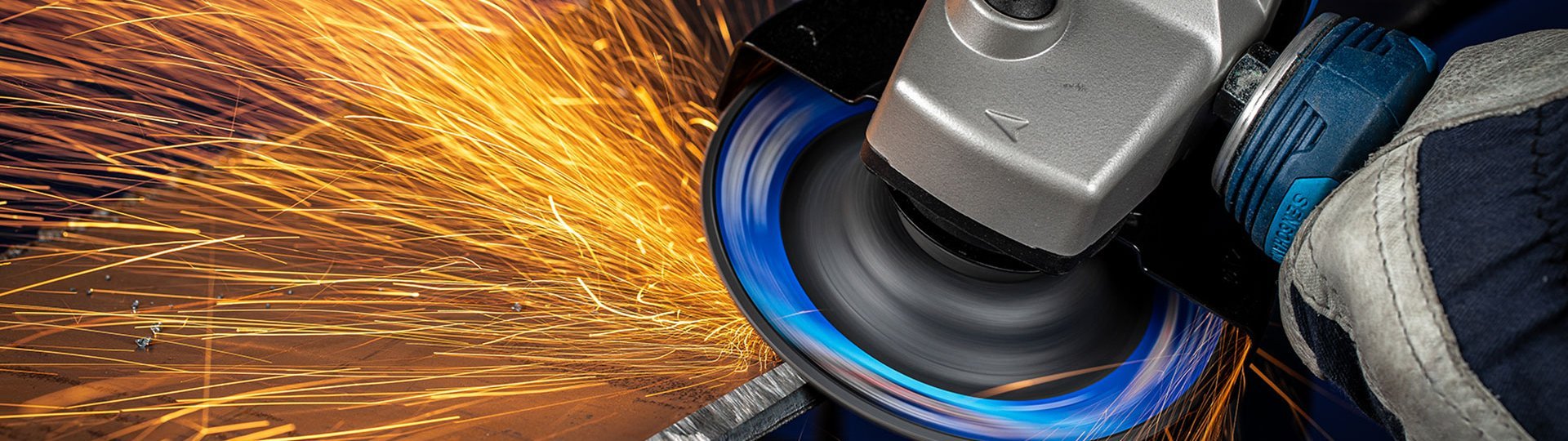 Grinding machine works on metal and sprays sparks, hand with protective glove holds the tool.