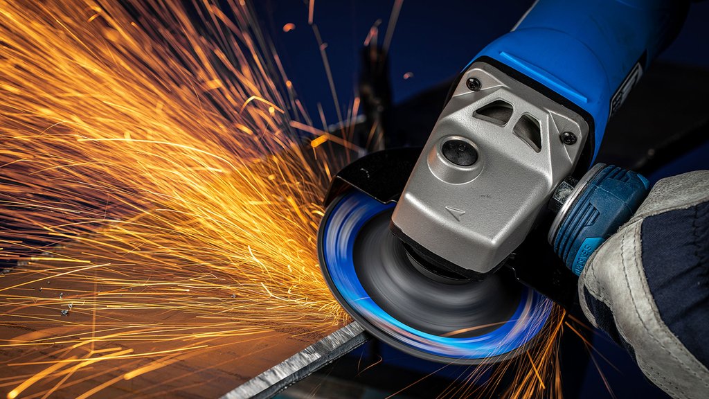 Grinding machine works on metal and sprays sparks, hand with protective glove holds the tool.