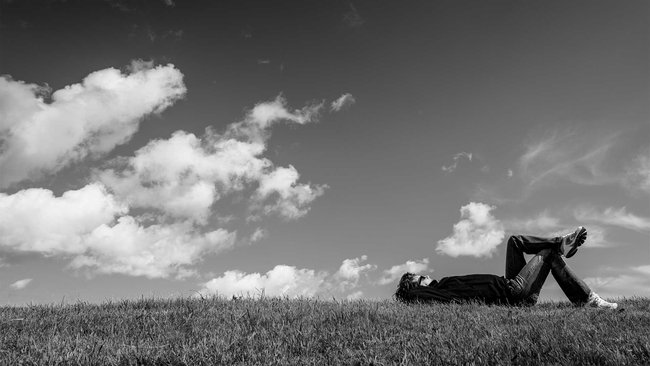 Person lying relaxed on a meadow and looking up at the sky with clouds.