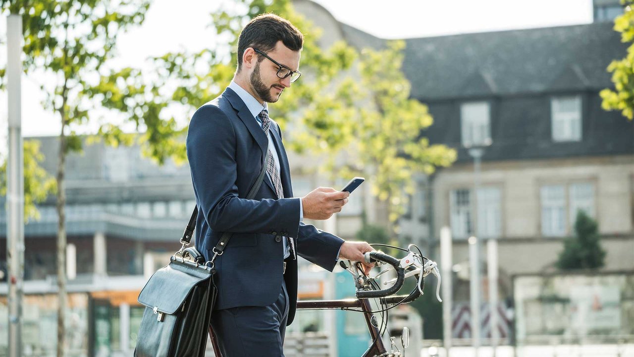 Businessman in suit pushing bicycle and looking at smartphone in urban environment.