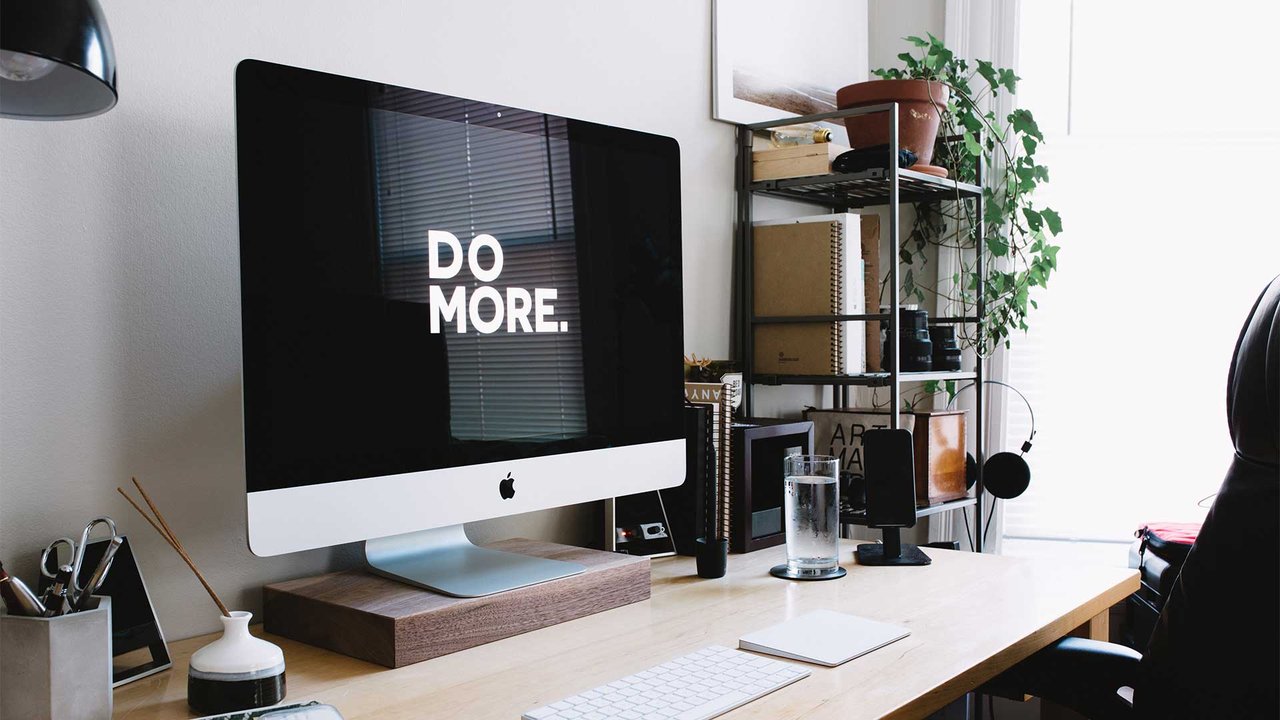 A modern desk with an iMac, “DO MORE” screen and minimalist furnishings.