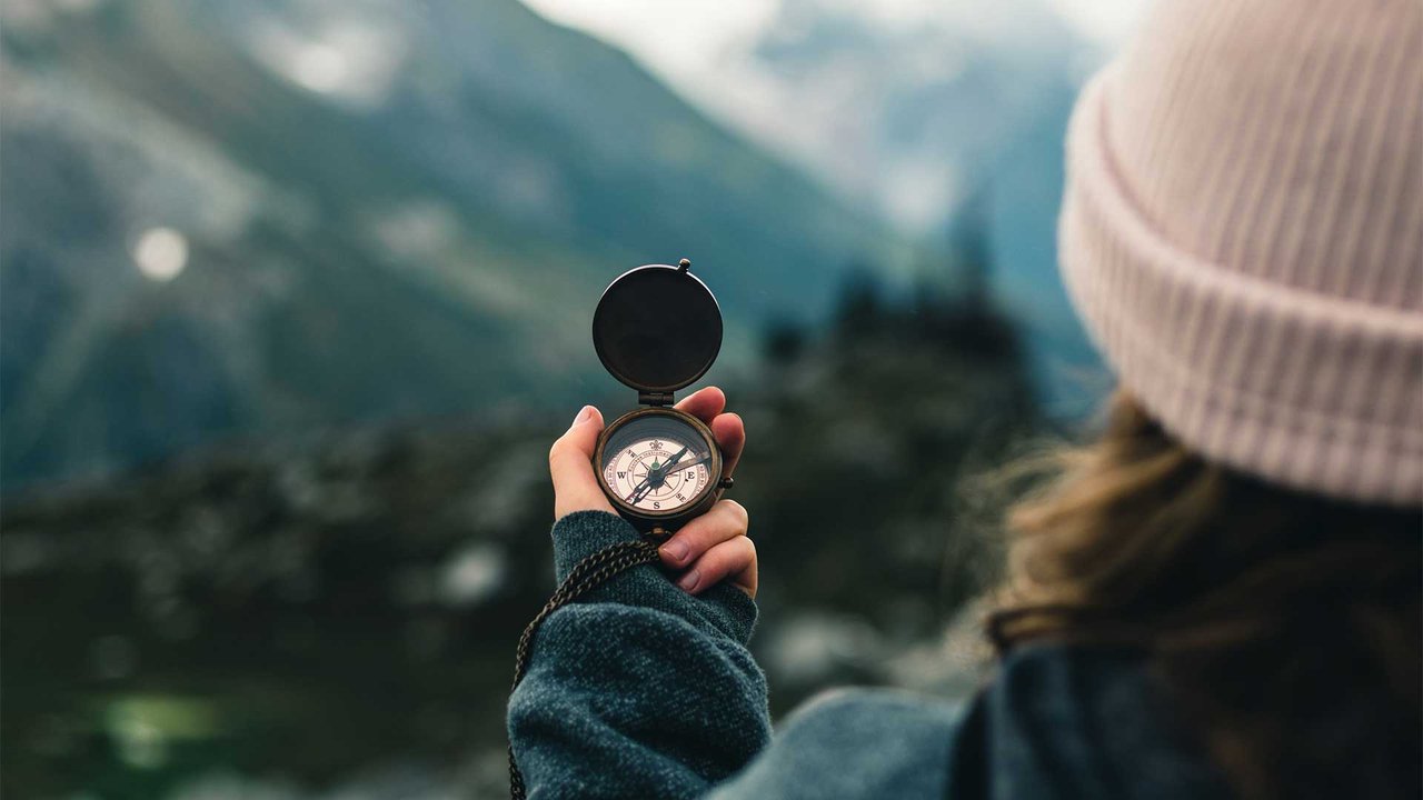 Person holding a compass and looking at a mountain landscape for orientation.