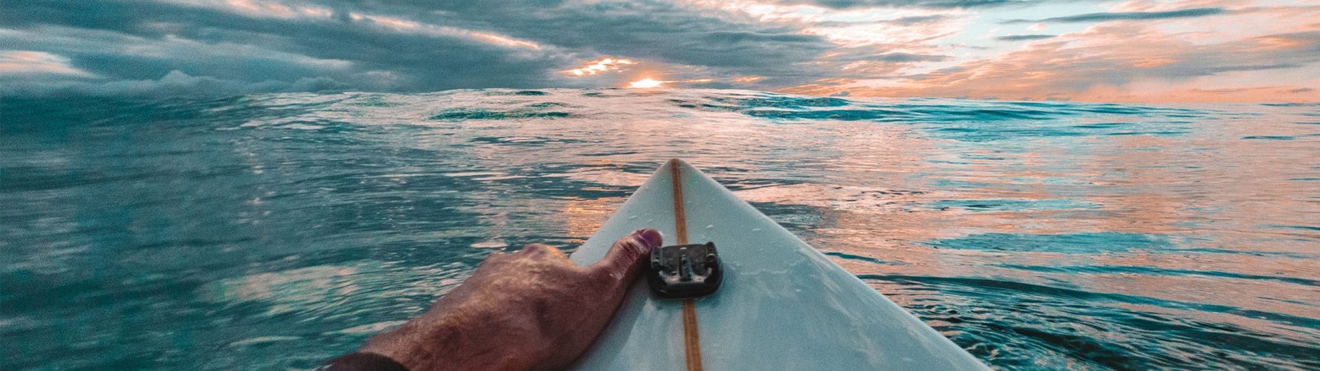 Surfer on board paddling over calm sea at sunset, view of colorful sky.