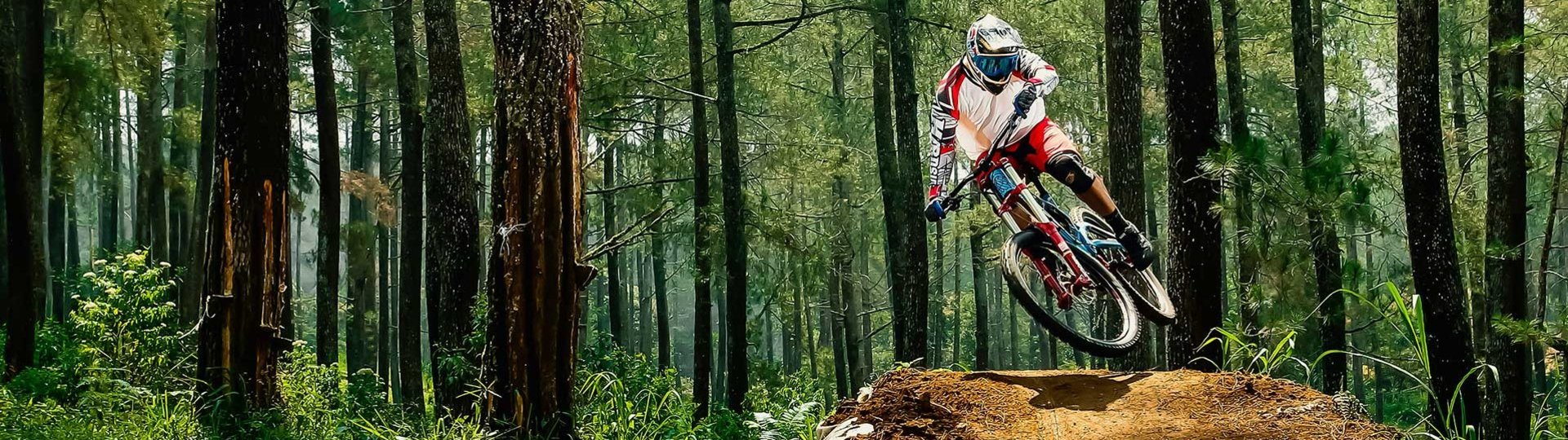 Mountain biker jumping over a mound of earth on a forest track in daylight in a sporty pose.