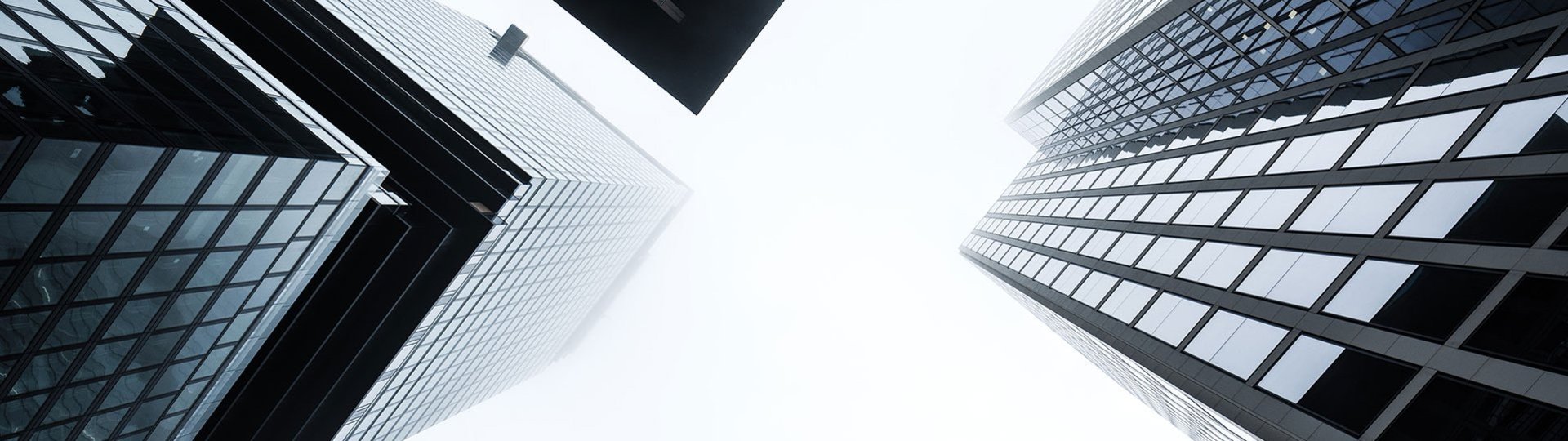 View upwards to glass facades of skyscrapers against a misty sky, urban architecture.