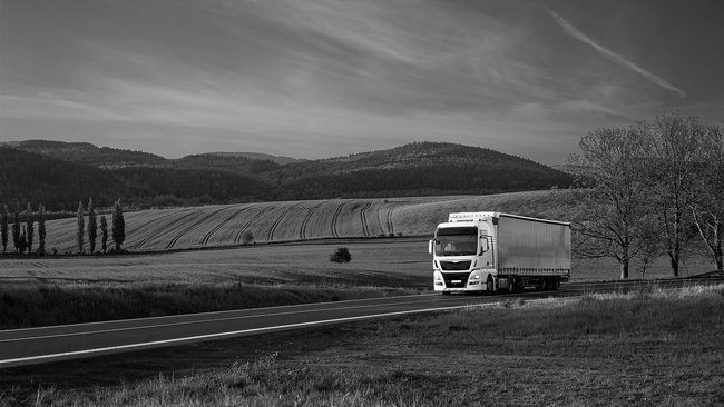 White truck on a country road, surrounded by fields and hills, for sustainable logistics.