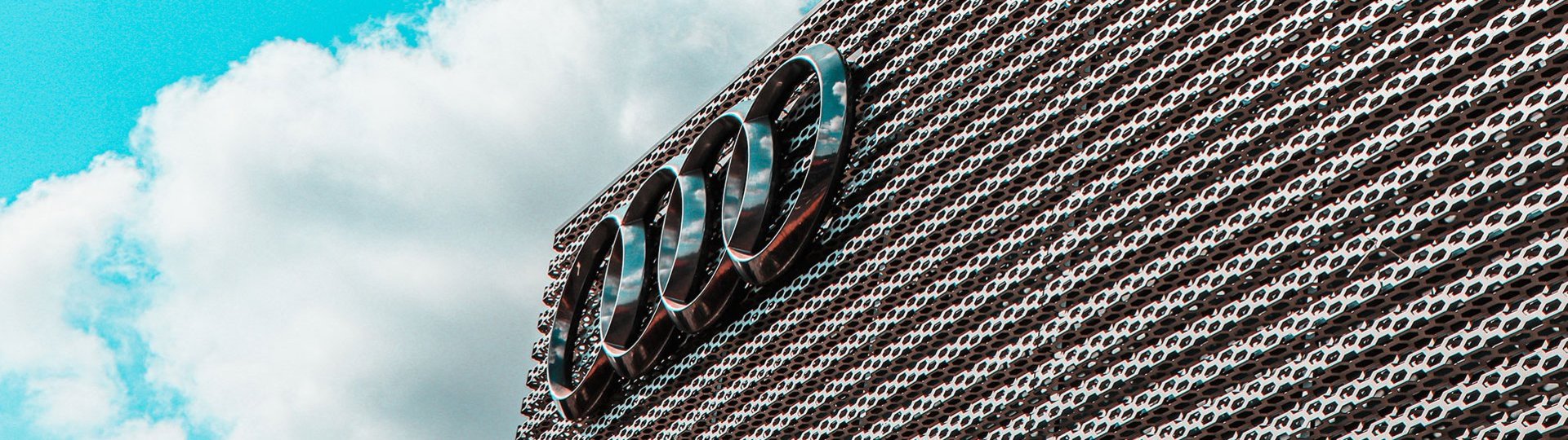 Audi logo on a modern building in front of a blue sky with white clouds.