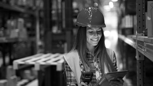Warehouse worker with helmet uses tablet and scanner to manage stock in the warehouse.
