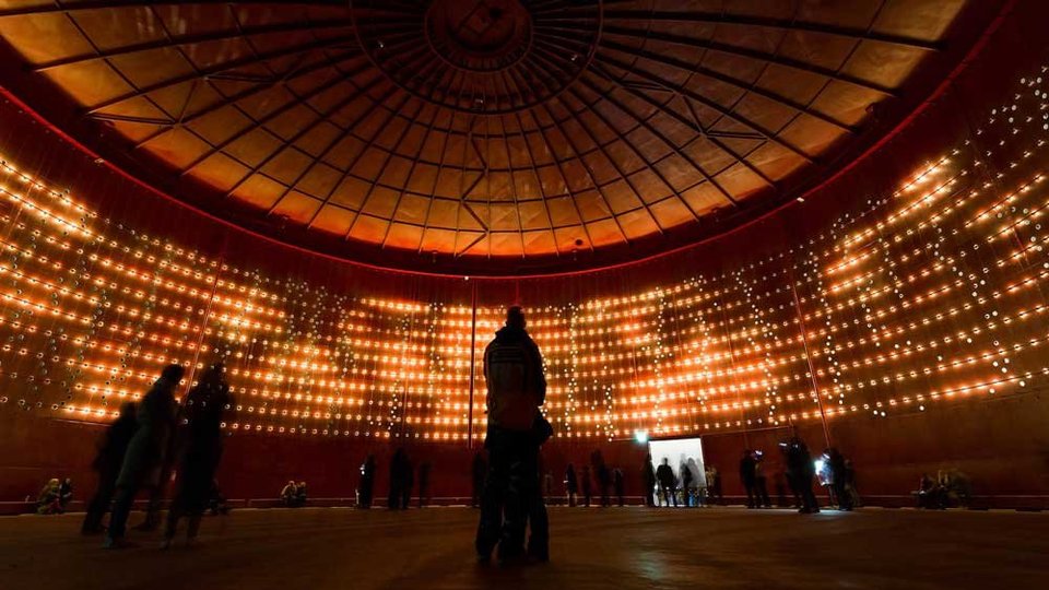 Dome-shaped room with people looking at a light installation consisting of many small light bulbs.