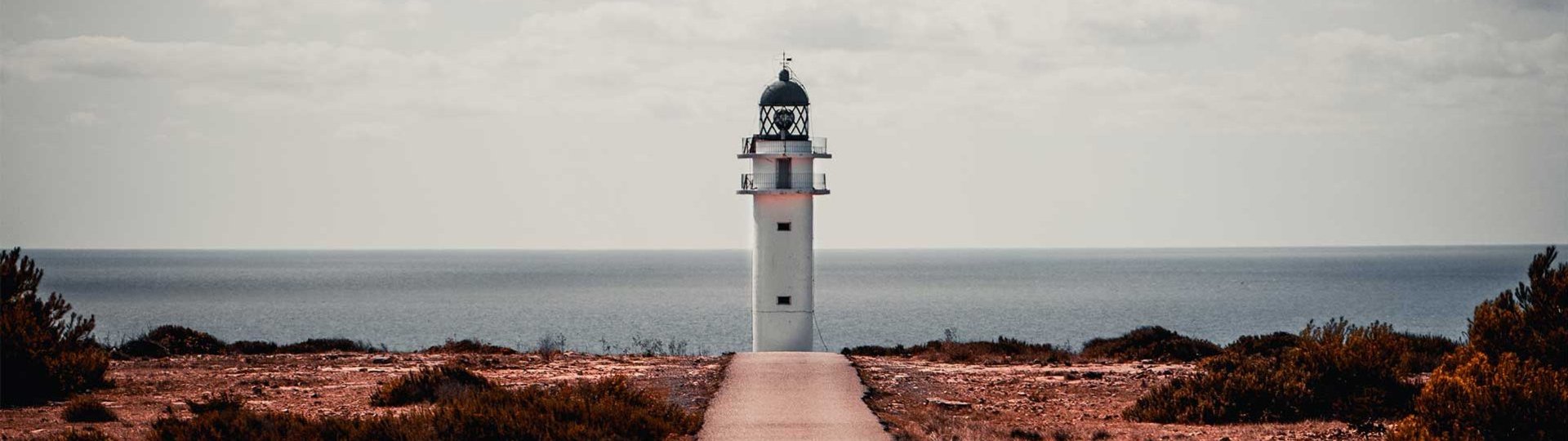 Lonely lighthouse at the end of a path with the sea in the background.