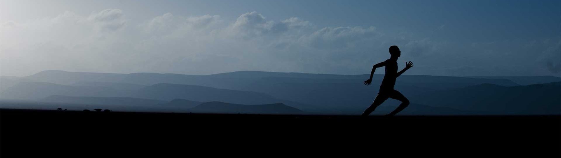 Silhouette of a runner in front of a misty mountain landscape and clear sky, dynamic scene.