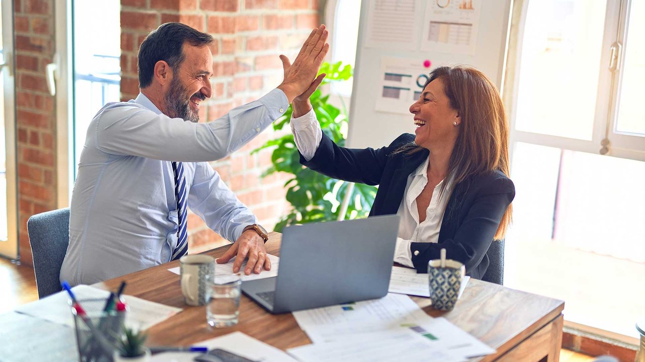Two business people give each other a high-five in the office after a successful collaboration.