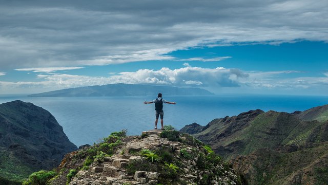 A hiker on a mountain peak with a view of the sea and distant island. 