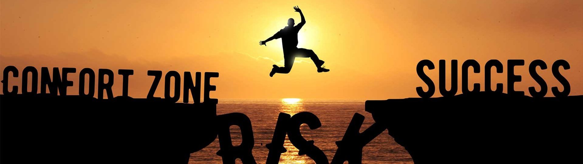 Silhouette jumps from “Comfort Zone” to “Success” over “Risk” abyss at sunset.