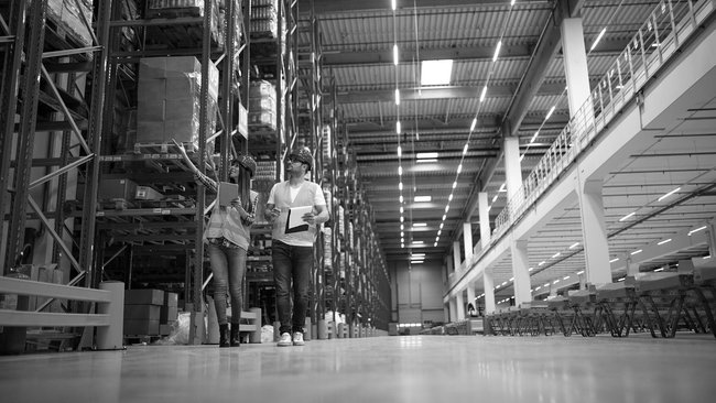 Two warehouse workers with tablets inspect high-bay warehouse for stock control.