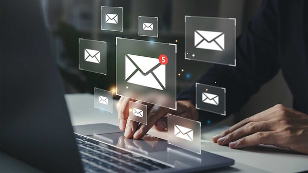 Hand taps on laptop keyboard to manage emails with five unread messages.