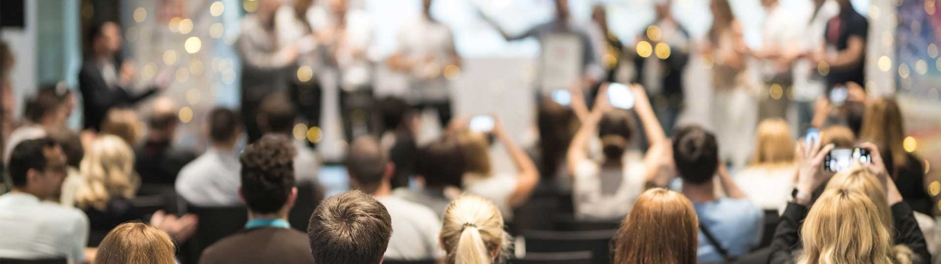 Participants at an award ceremony, several people take photos of the award on stage.